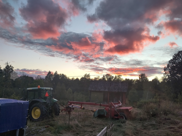Traktor och slåttermaskin framför ein kvällshimmel med röda och gråa moln